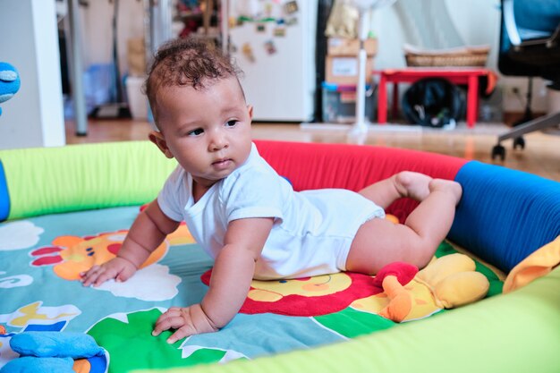 Schattige babyjongen liggend op zijn buik op een kleurrijke speelmat thuis.