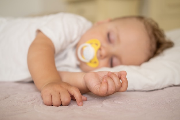 Schattige babyjongen met tepel slapen op bed thuis. selectieve focus op handen.