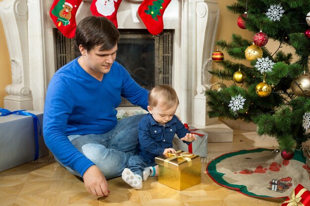 Schattige babyjongen met zijn vader die kerstcadeaus opent op de vloer in de woonkamer