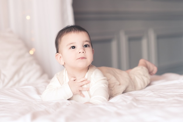 Schattige babyjongen onder de 1 jaar oud wordt wakker in bed met een stijlvolle pyjama close-up. Wegkijken. Jeugd. Goedemorgen.