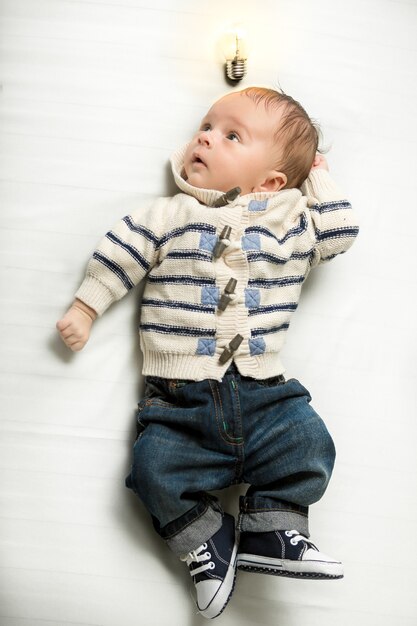 Schattige babyjongen poseren op bed met gloeiende gloeilamp overhead