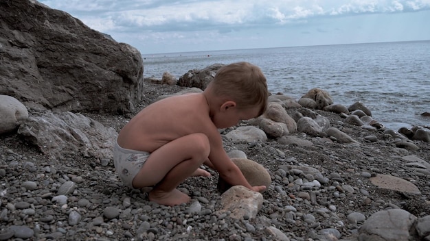 Schattige babyjongen spelen aan de kust met rotsen en kiezels Het kind heeft een goede tijd op een familievakantie Slow motion video