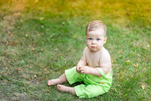 Schattige babyjongen zittend op een groen gazon in de zomer met grote blauwe ogen, een plek voor tekst.