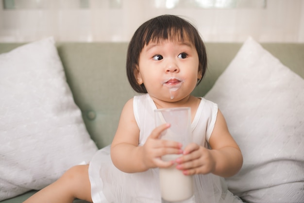 Schattige babymeisje consumptiemelk met melk snor thuis