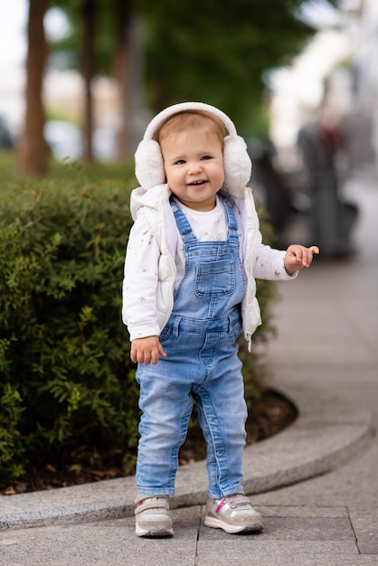 Schattige babymeisje draagt donzige witte koptelefoon denim pak broek en gebreide trui