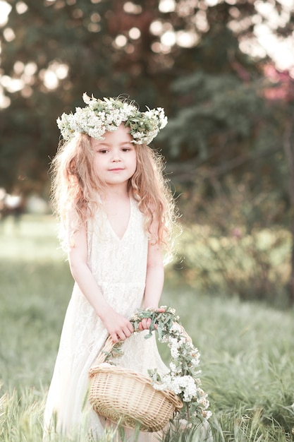 Schattige babymeisje dragen witte jurk en bloemenkrans buitenshuis