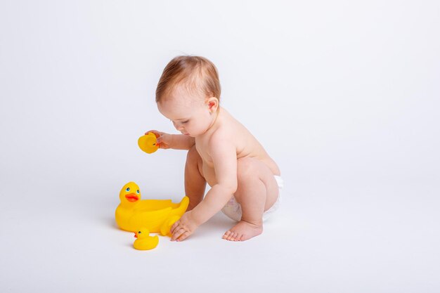 Schattige babymeisje in een luier spelen met een rubberen speelgoed eend geïsoleerd op een witte achtergrond