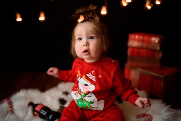 Schattige babymeisje in een rode kerst kostuum met retro slingers zit op een vacht
