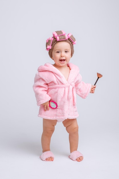 Schattige babymeisje in roze badstof met make-up geïsoleerd op een witte achtergrond herhaalt het gedrag van mama