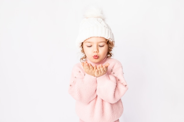 Schattige babymeisje in roze winterkleren op een witte achtergrond waait uit haar handen, ruimte voor tekst