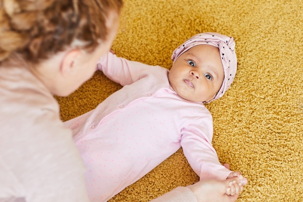 Schattige babymeisje liggend op de vloer terwijl vrouw haar oefeningen doet