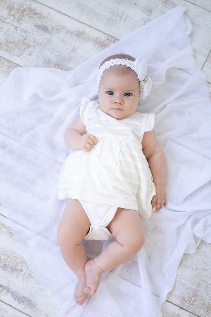 Schattige babymeisje met blauwe ogen in witte kleren liggend op haar rug op een witte achtergrond kijken naar de camera