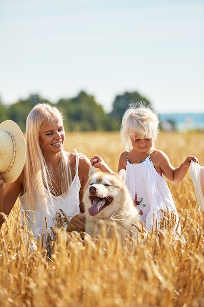 Schattige babymeisje met moeder en hond op tarweveld. Gelukkig jong gezin genieten van tijd samen in de natuur.