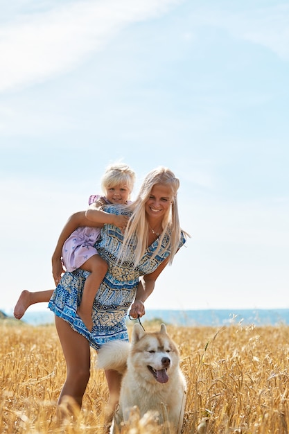 Schattige babymeisje met moeder en hond op tarweveld