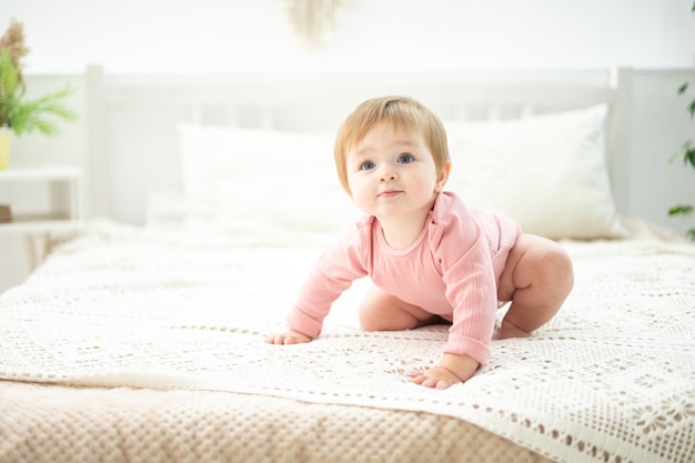 Schattige babymeisje zit op een bed met wit linnengoed in de slaapkamer van het huis een kinderportret het kind kijkt naar de camera