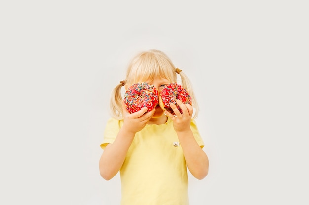 Schattige babymeisje zoete donuts eten op een lichte achtergrond.