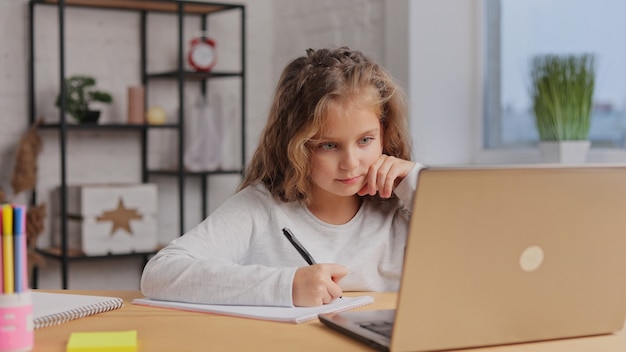 Schattige basisschool meisje thuis studeren met behulp van laptopcomputer. Afstandsonderwijs, thuisonderwijs