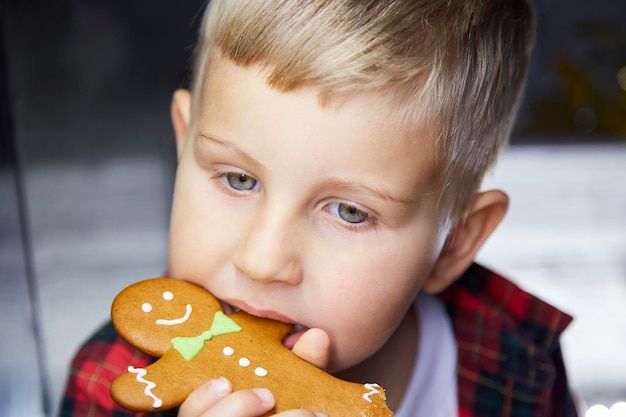 Schattige blanke jongen eet peperkoek en maakt een grappige gezichtsuitdrukking Kerst eten Sfeervol esthetisch kersthuis voor oudejaarsavond 39s Vrolijke babyjongen Vrolijk goed humeur