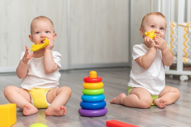 Schattige blije baby's spelen samen op de grond met speelgoed en nemen ze in hun mond