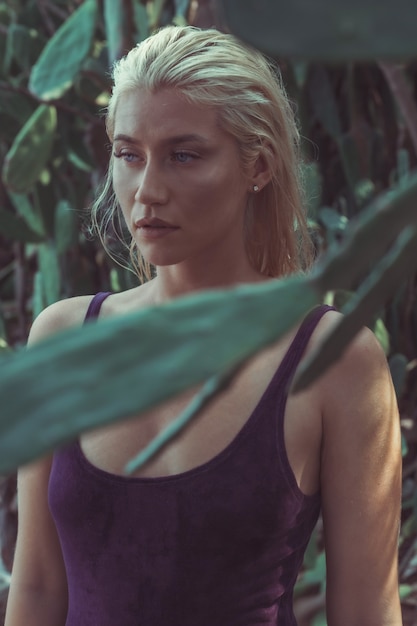 Schattige blonde dame staande tussen het cactusveld in Koh Larn Island, Thailand in een fluwelen jurk en opzij kijkt.