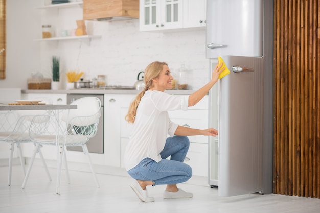 Schattige blonde huisvrouw die de koelkast schoonmaakt en er druk uitziet