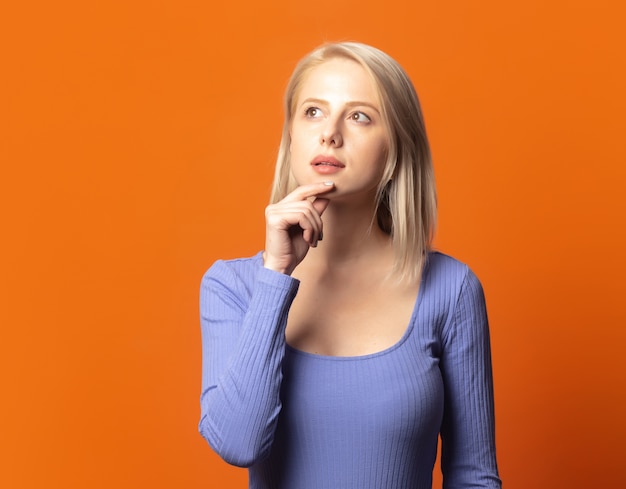 Schattige blonde in blauwe blouse op een uitbundige oranje kleur achtergrond