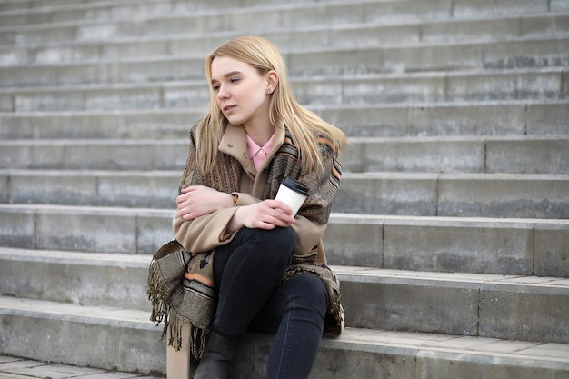 Schattige blonde in de stad die koffie drinkt op de trap