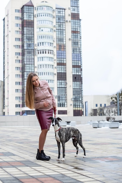 schattige blonde meid houdt een whippet-hond aan de lijn in de stad