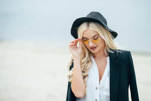 Schattige blonde meid met een bril loopt langs de kust en geniet van het leven