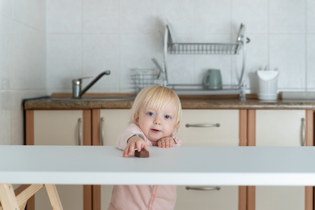 Schattige blonde meisje trekt haar hand naar snoep op tafel.