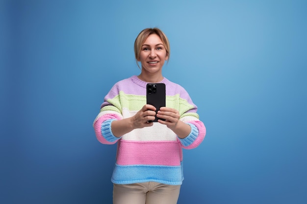 Schattige blonde vrouw in een nonchalante look maakt een foto op een smartphone op een blauwe achtergrond