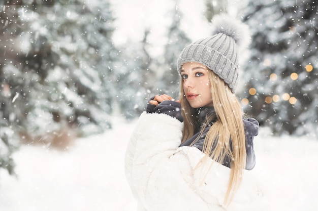 Schattige blonde vrouw in een witte jas wandelen in het bos bij sneeuwweer. ruimte voor tekst