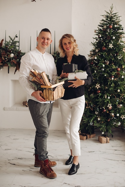 Schattige blonde vrouw met geschenkdozen terwijl ze in de buurt van haar partner staat en recht in de camera kijkt