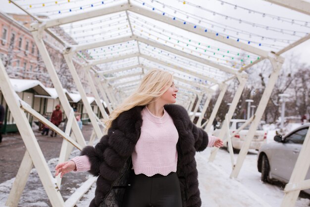 Schattige blonde vrouw met lichte make-up poseren op straat in de winter