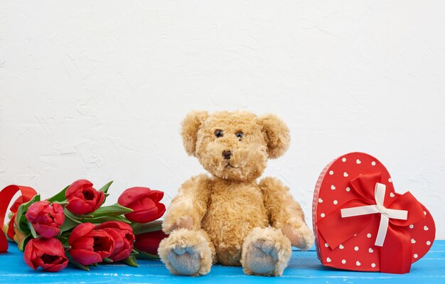 Schattige bruine teddybeer zit, boeket rode tulpen, rode doos