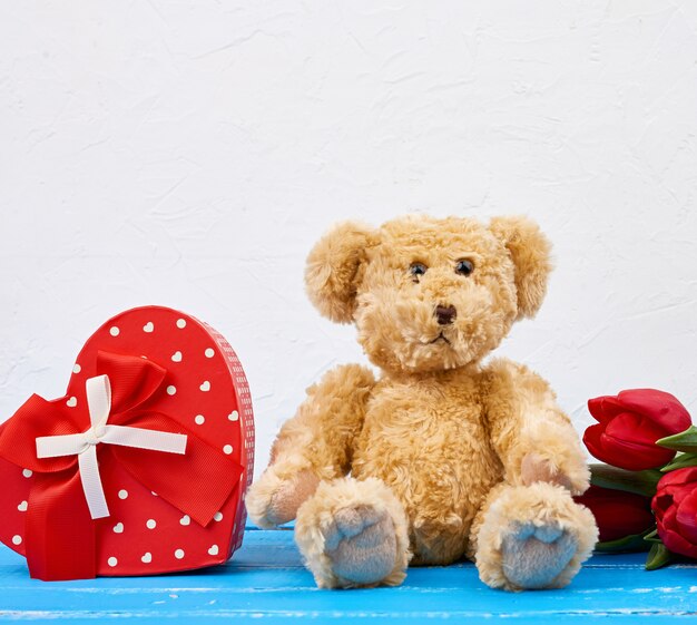 Schattige bruine teddybeer zit, boeket van rode tulpen