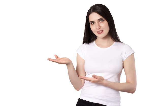 Schattige brunette lachende vrouw in wit t-shirt op witte achtergrond handen verhoogd commerciële aanbieding