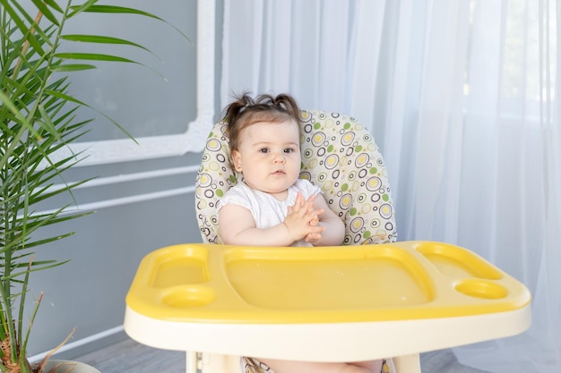 Schattige dikke babymeisje zittend in een hoge stoel aan een lege tafel en wachten op voedsel babyvoeding concept