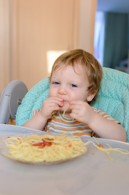 Schattige een jaar oude baby eet spaghetti in een kinderstoel.