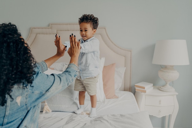 Schattige gelukkige kleine Afro-Amerikaanse jongen spelen met zijn moeder in de slaapkamer thuis