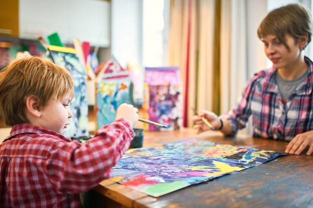 Schattige gelukkige kleine jongen en leraar tekenen in de kunstenaar klasse.