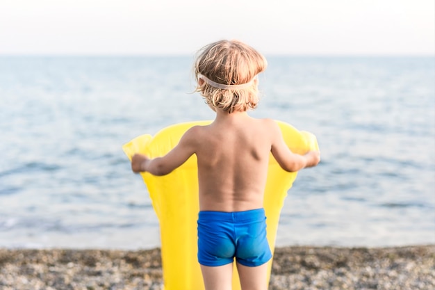 Schattige grappige kleine jongen spelen met gele matras zwemmen op zee kust zomer strand vakantie kind...