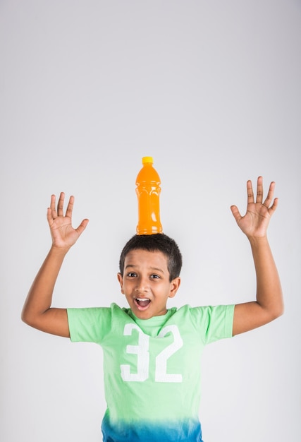 Schattige Indiase of Aziatische kleine jongen jongen met een huisdier fles sinaasappel of mango koud drankje of vruchtensap, drinken of vasthouden terwijl staande geïsoleerd over blauwe of witte achtergrond.