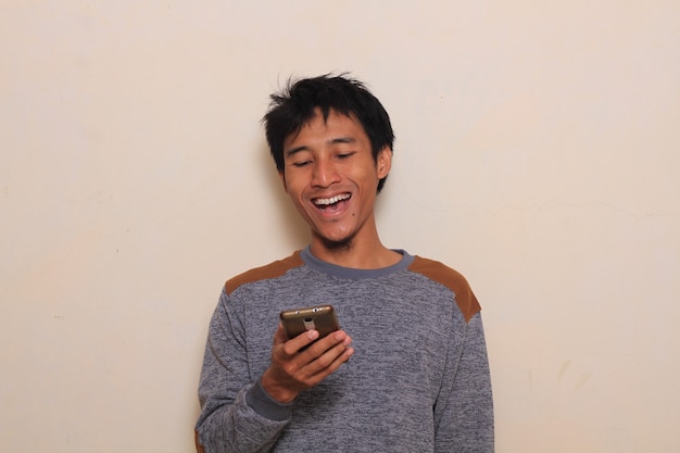 schattige jonge Aziatische man verrast, glimlach na het kijken naar zijn smartphone. geïsoleerd met warme bac