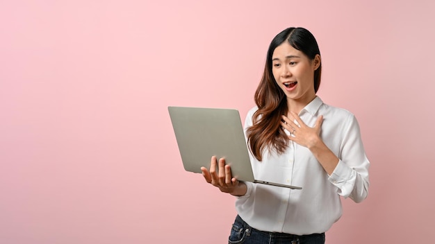 Schattige jonge Aziatische vrouw die zich verrast voelt terwijl ze naar een laptop geïsoleerde achtergrond kijkt