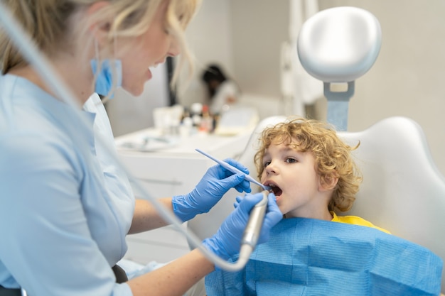 Schattige jonge jongen bezoekende tandarts en het hebben van zijn tanden gecontroleerd door vrouwelijke tandarts in tandartspraktijk