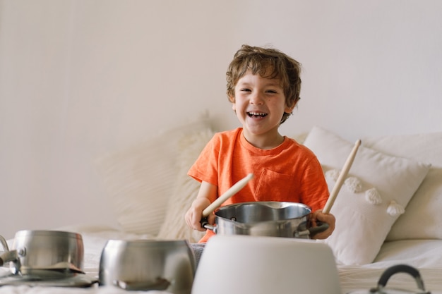 Schattige jonge jongen die houten stokken gebruikt om pannen te slaan die zijn opgesteld als een drumstel