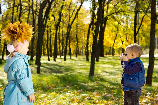 Schattige jonge jongen fotografeert de herfsthoed van zijn zus gemaakt van een verzameling kleurrijke gele herfstbladeren verzameld