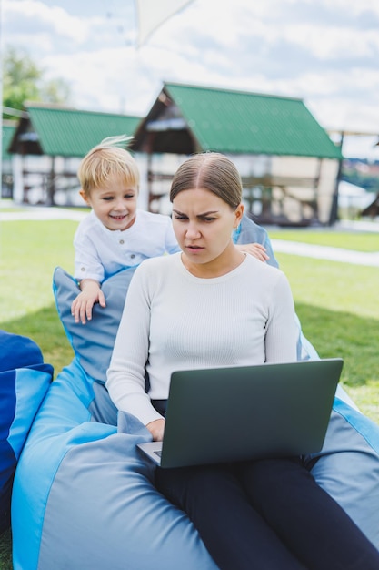 Schattige jonge moeder en zoon kijken naar laptop Gelukkige familie moeder en zoon rusten in het park Een vrouw met zwangerschapsverlof