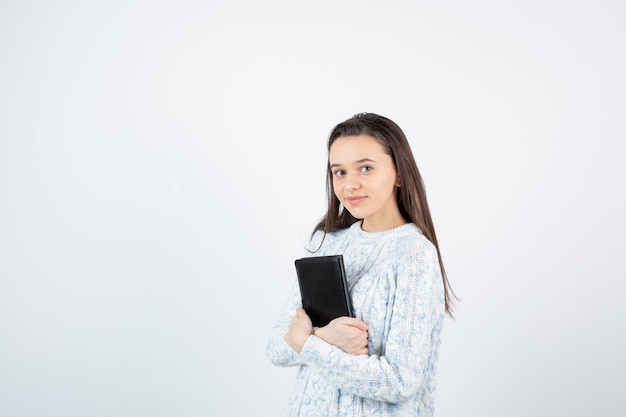 schattige jonge student poseren met notebook op witte muur.